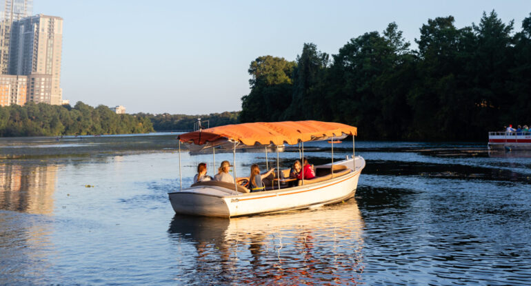 Covered Capital Cruises-style boat on Lady Bird Lake at sunset in Austin